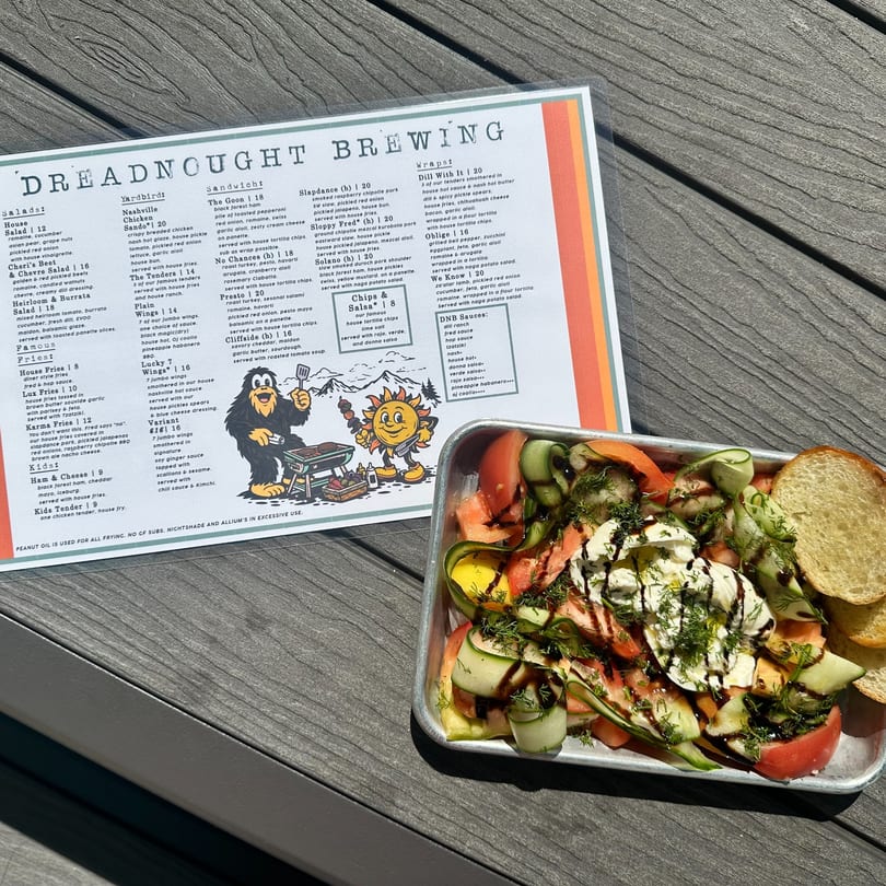 A Dreadnought Brewing menu and a metal tray of Heirloom & Burrata Salad with toasted panette slices.